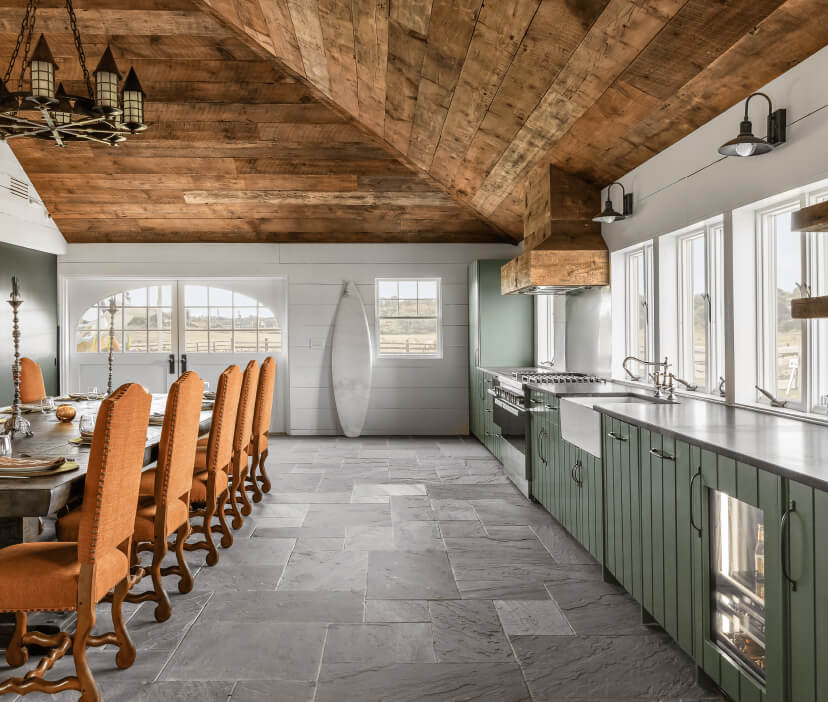 Open kitchen with green cabinetry, stone flooring, custom wood vent hood and a spacious dining table for entertaining.