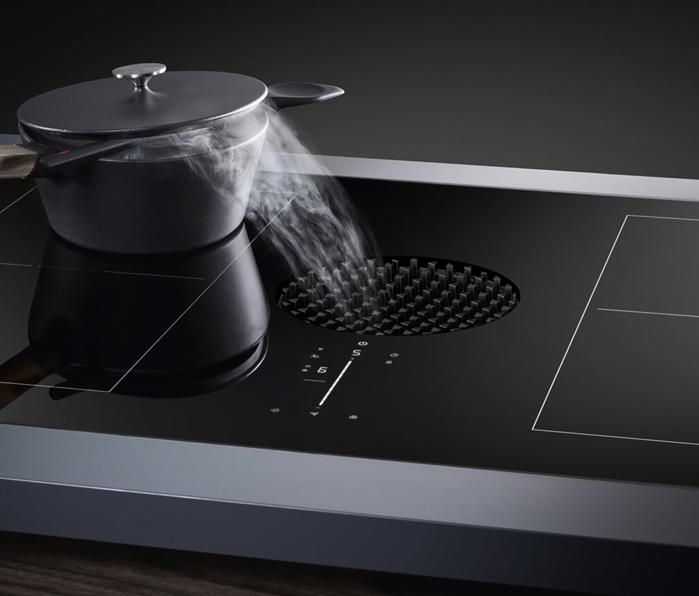 A lidded pot with steam coming out on a JennAir® Induction Downdraft Cooktop.