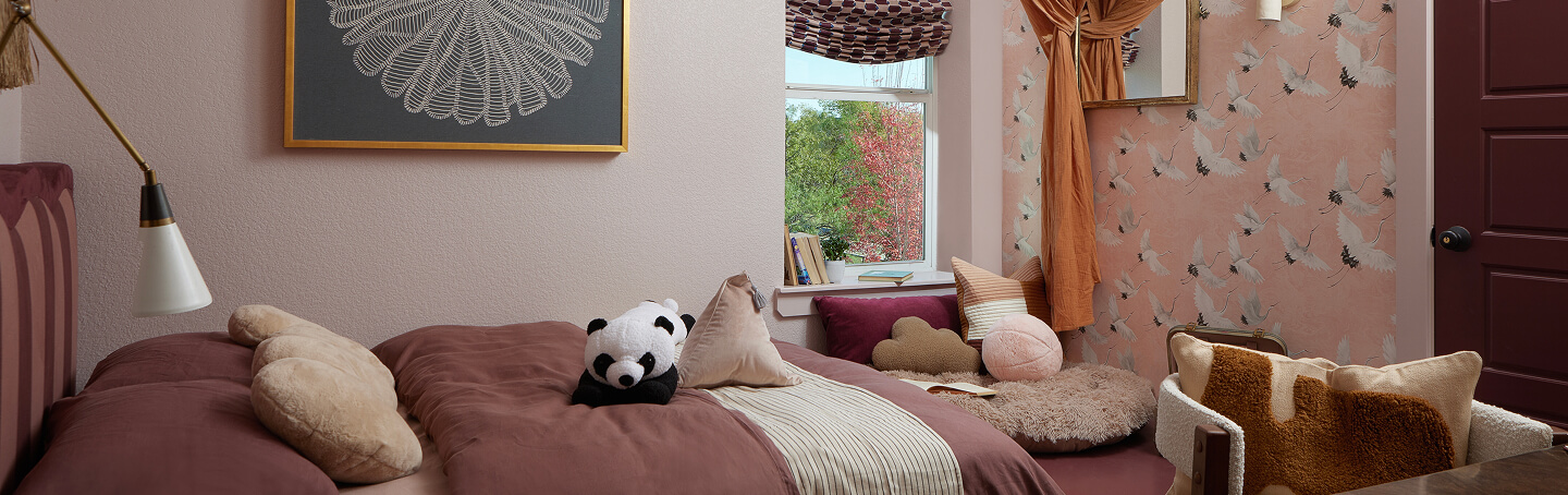 A bright bedroom with a plush panda and other pillows on the bed.