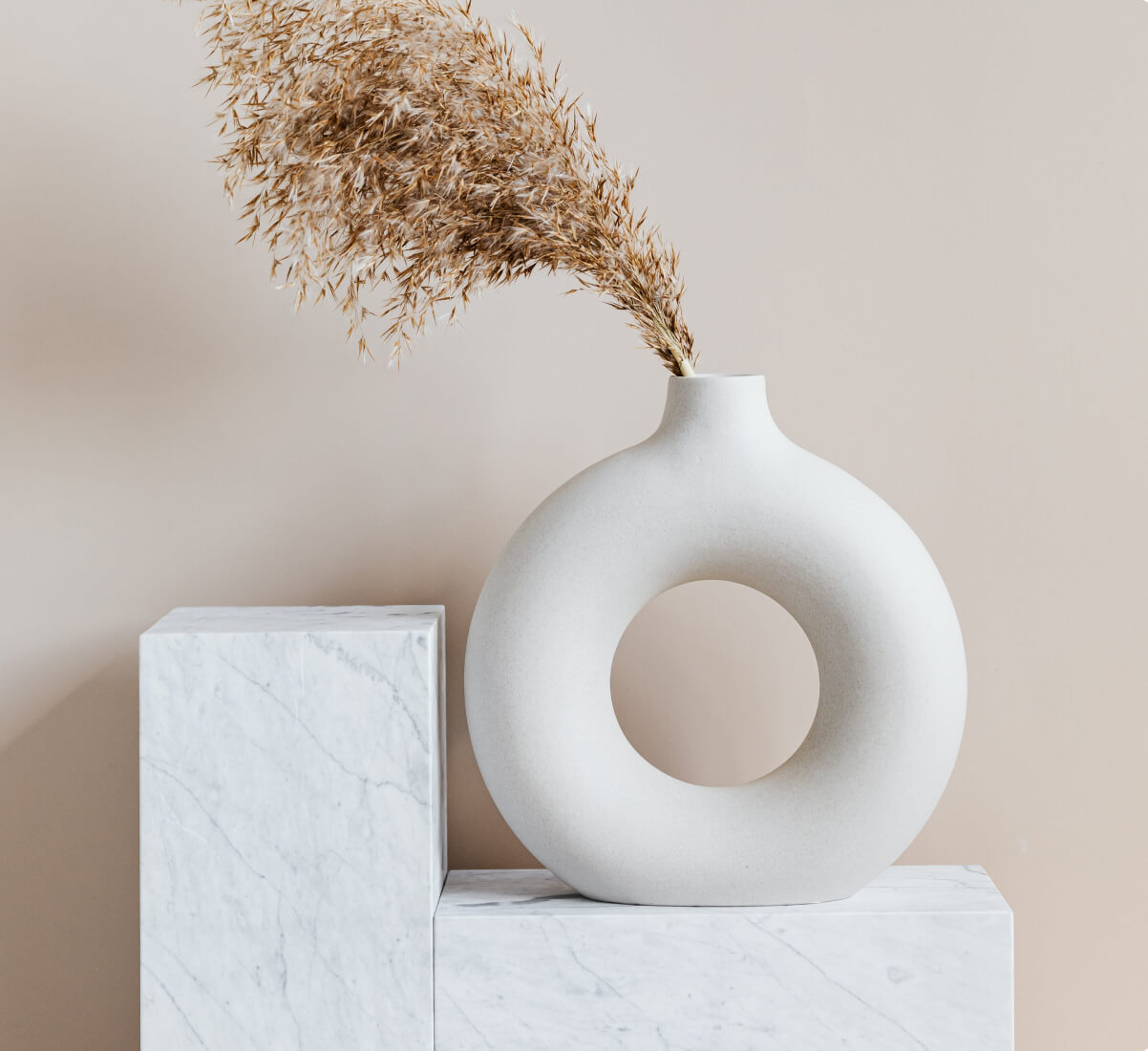 A round, donut-like vase sitting on a stone display platform with dried florals in it.