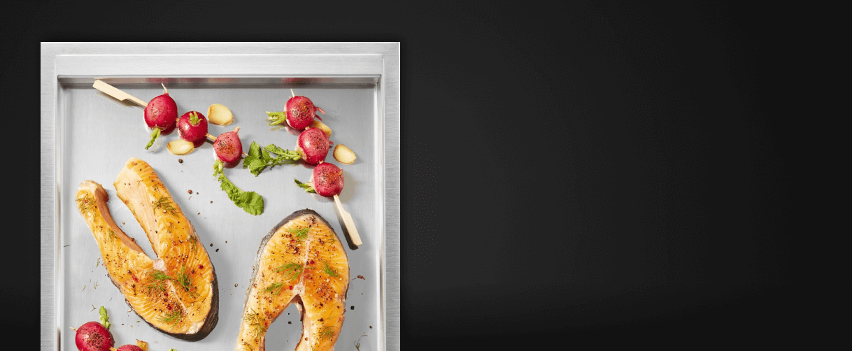A close up of the griddle surface with salmon steaks and cherry tomato skewers on it.