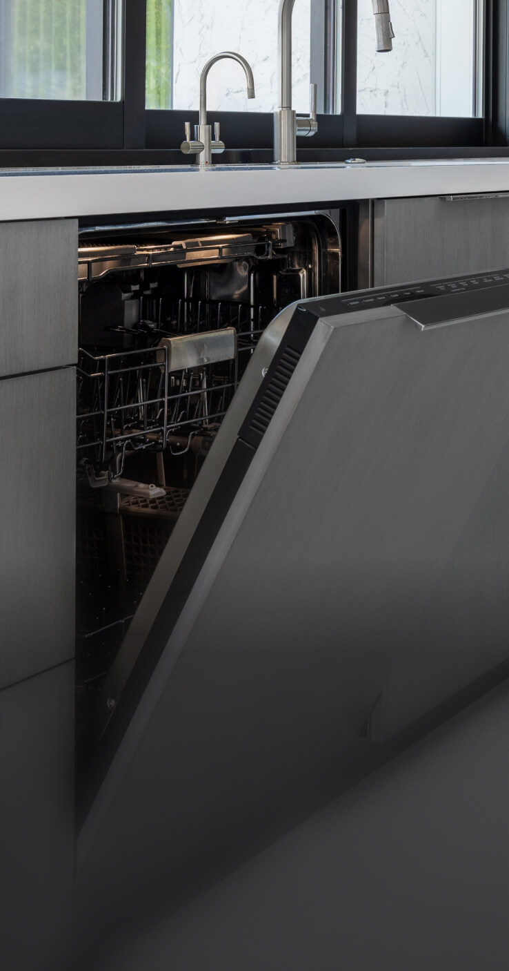 A JennAir® Panel-Ready Dishwasher with its door slightly ajar in a kitchen with gray cabinets.