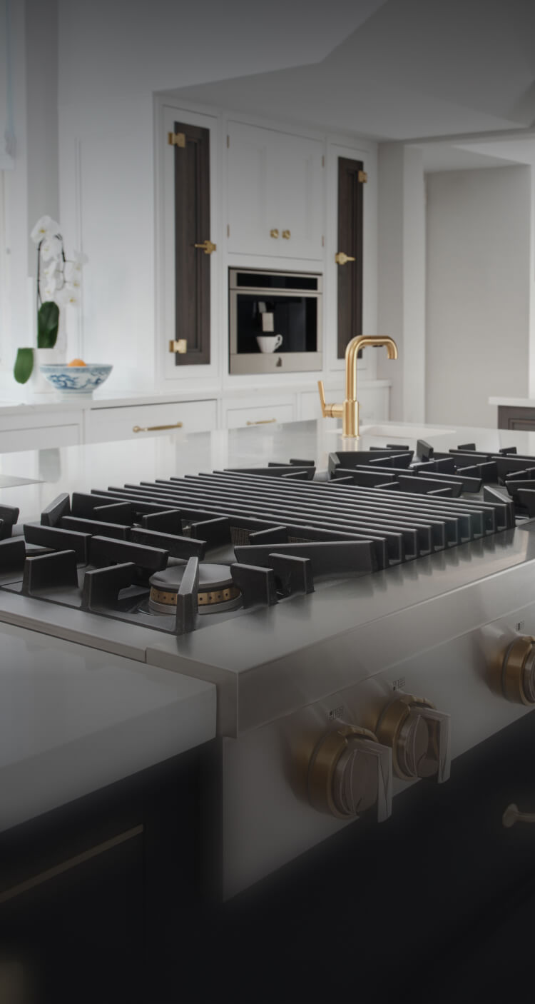 A JennAir® Gas Rangetop in a kitchen with dark cabinets and brass accents.