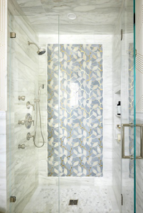 A white bathroom shower in marble with an accent tile wall.